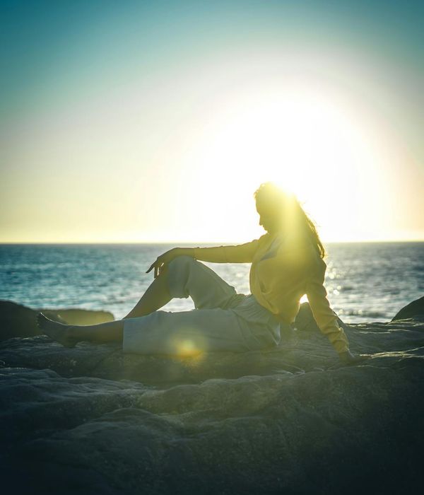 Person sitting in a meditative pose facing a beautiful sunrise over mountains.